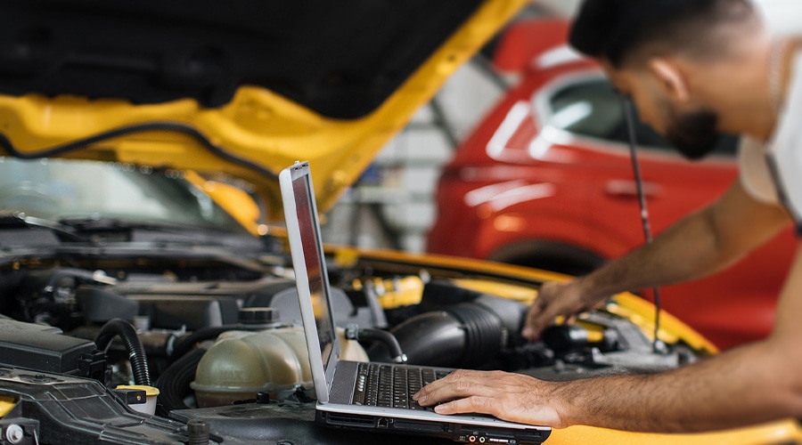 Close up of a mechanic under car hood checking engine with laptop using electronic diagnostic equipment to tune up vehicle.
